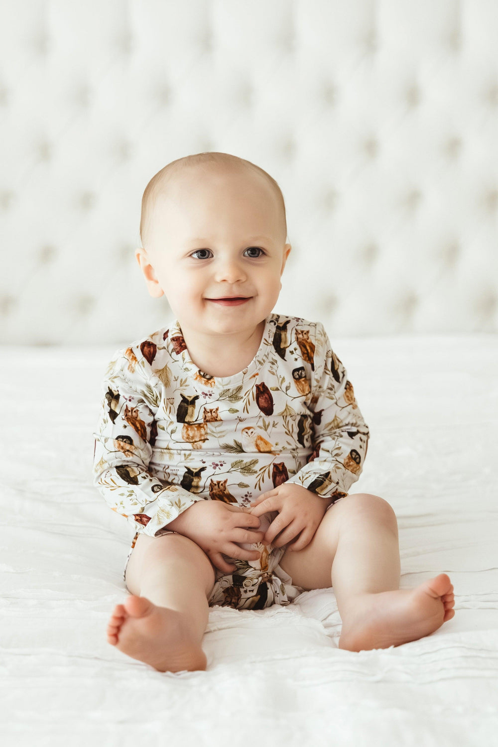 Front-facing baby sitting in Sleepy Hollow Owls bamboo bodysuit, smiling in cozy, unisex owl-themed outfit made for comfort and cuteness.