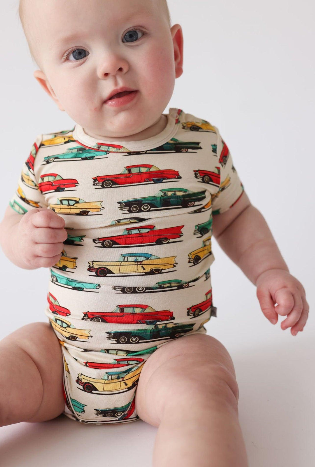 Baby sitting in classic cars short sleeve snap bottom bodysuit, smiling in a soft bamboo outfit perfect for warm weather.