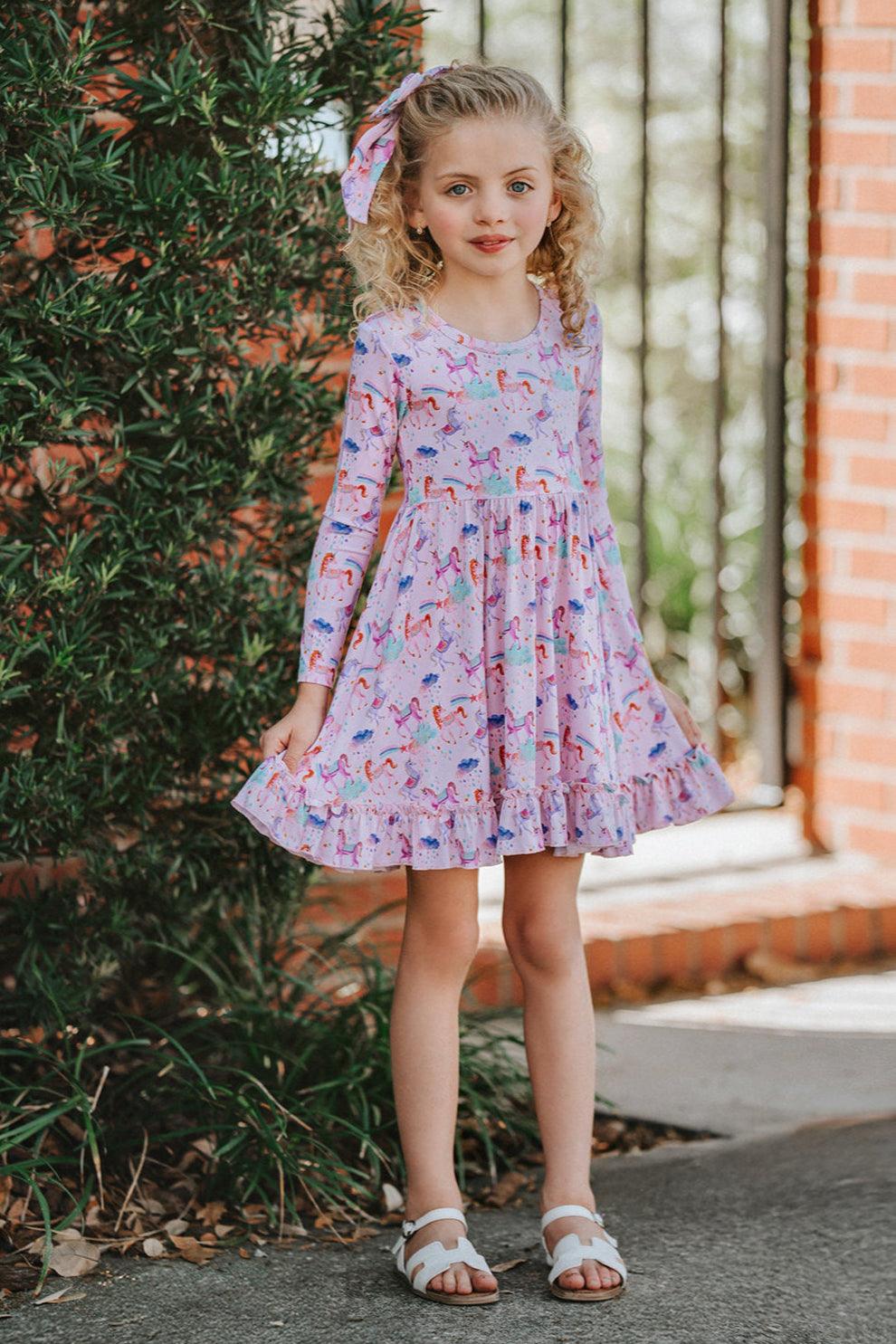 Little girl wearing Magical Unicorns long sleeve bamboo twirl dress, smiling outdoors in whimsical pink unicorn print — lightweight, stretchy, and perfect for school, parties, or play.