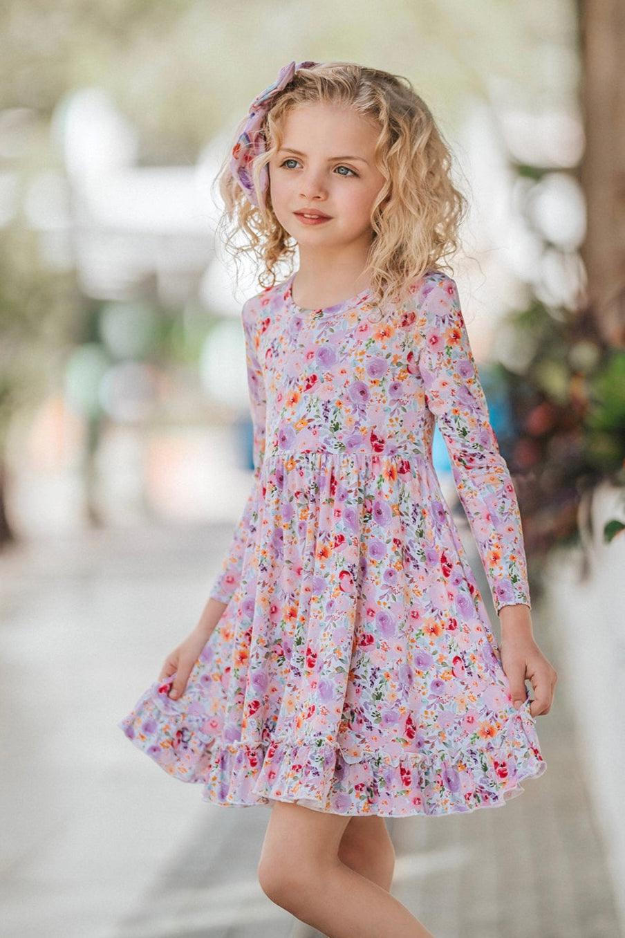 Girl wearing flower garden bamboo twirl dress with long sleeves and floral print, shown front-facing.