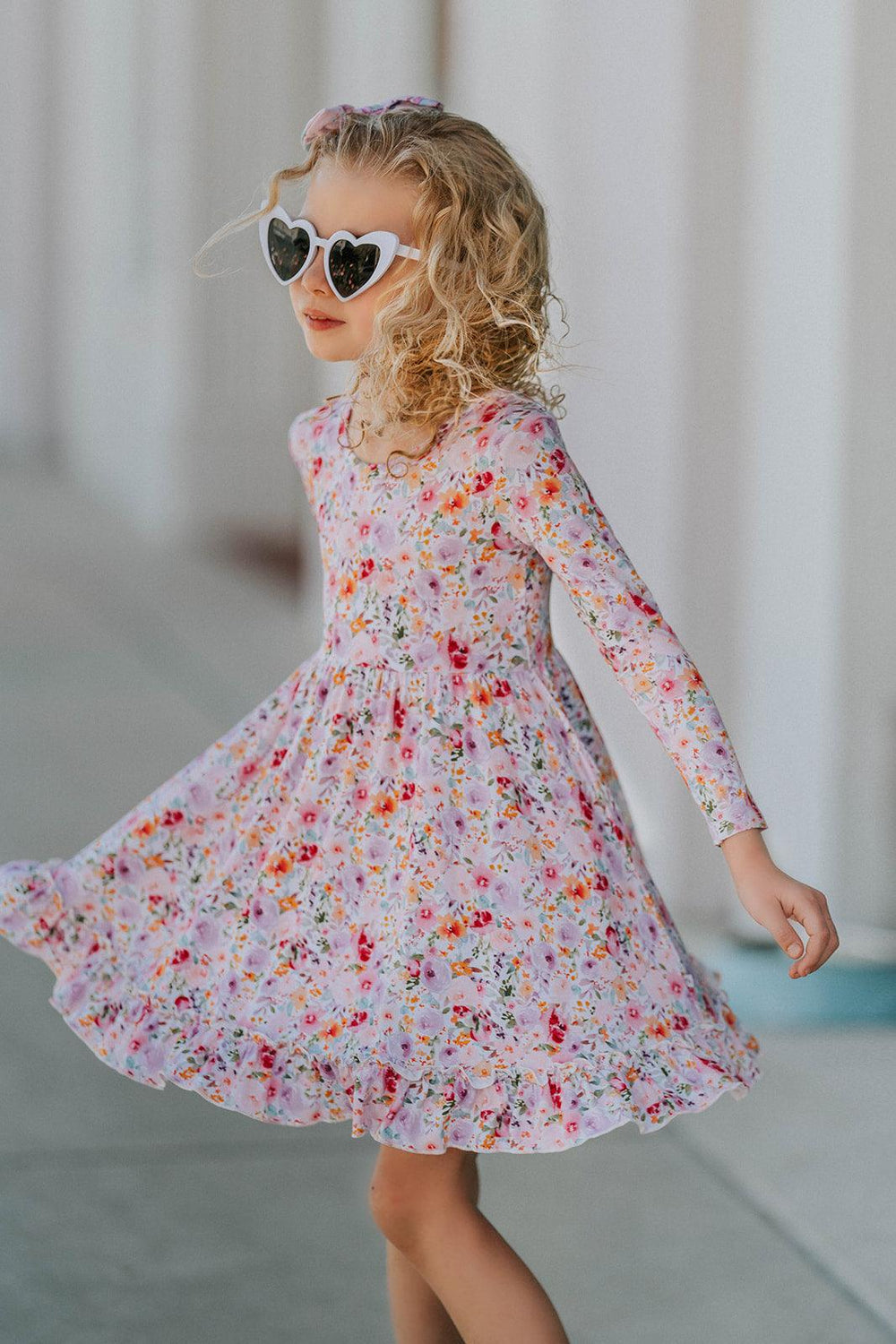 Front view of girl modeling bamboo floral twirl dress with ruffled hem and soft pastel color palette.