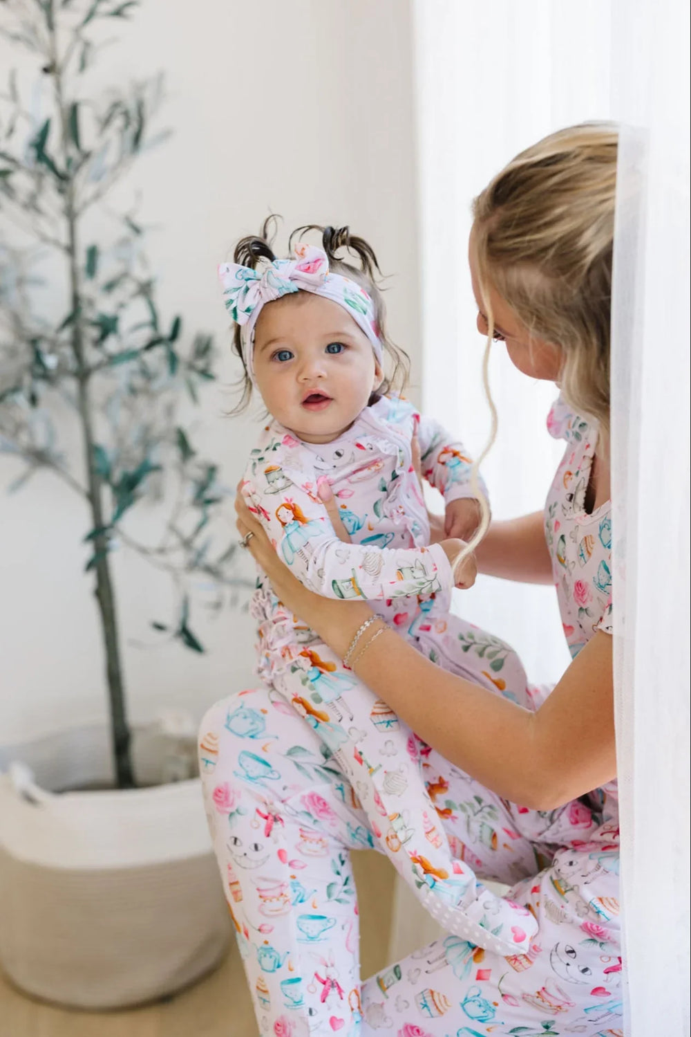 Mom and baby in matching Adventures with Alice bamboo pajamas, featuring pink print with teacups and Cheshire Cat.