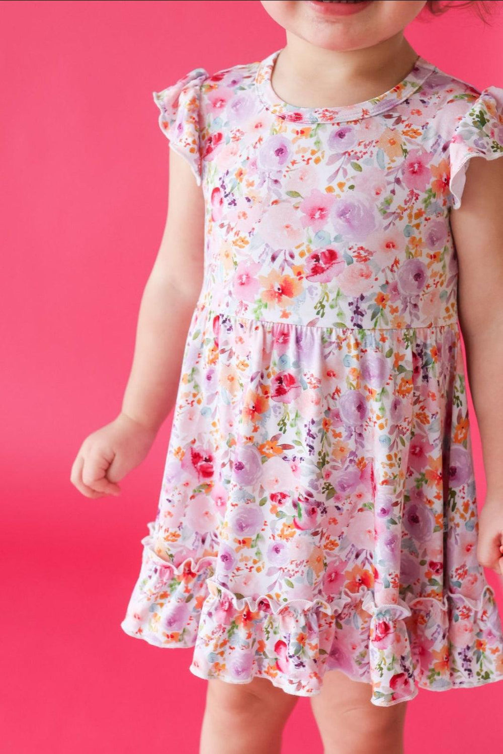 Front view of child in pink floral bamboo twirl dress with flutter sleeves and soft ruffle hem detail.