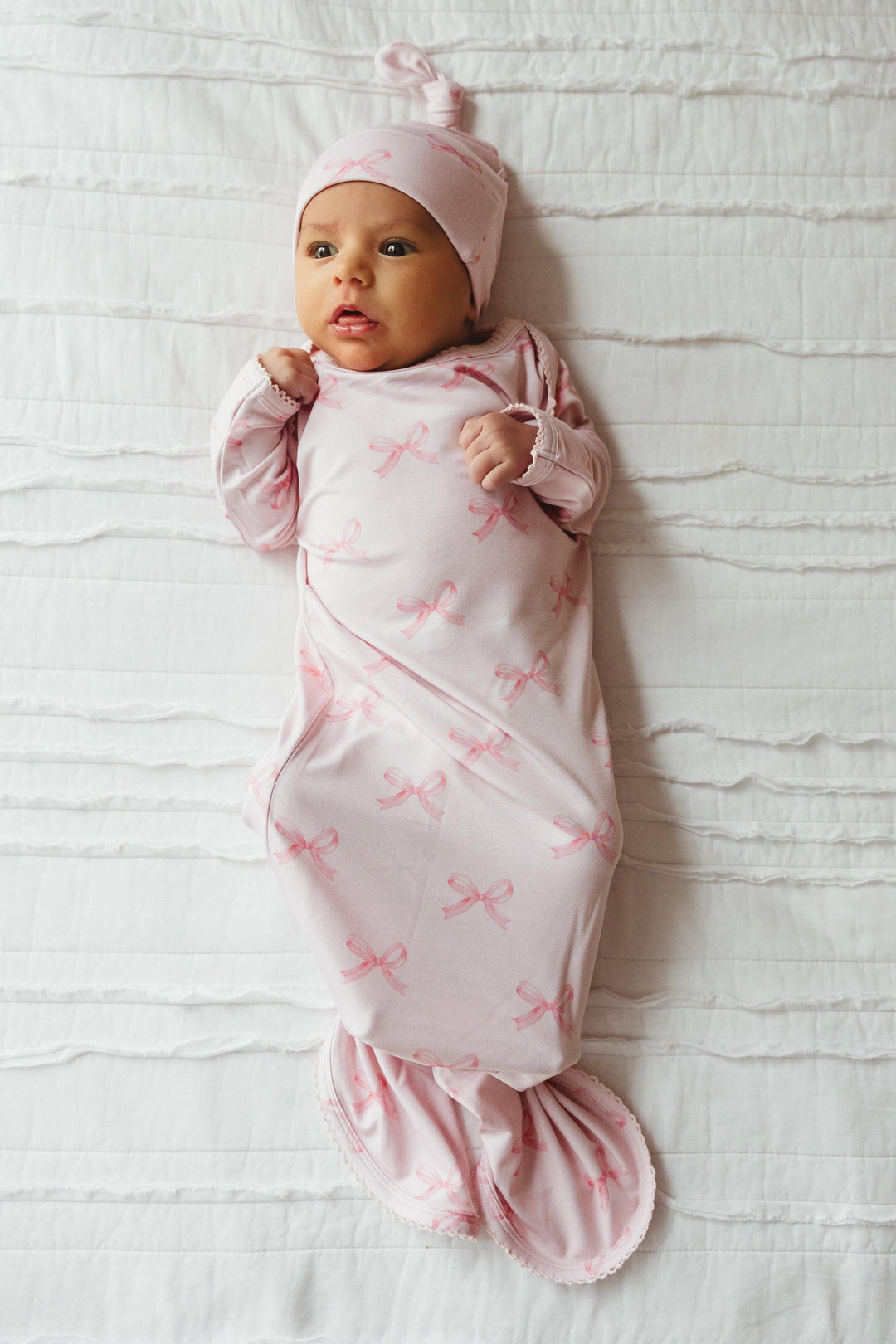 Newborn baby girl wearing pink bows bamboo knotted gown, featuring a light pink background with darker bow print and scalloped edging — soft, breathable, and perfect for newborn photos or gifting.