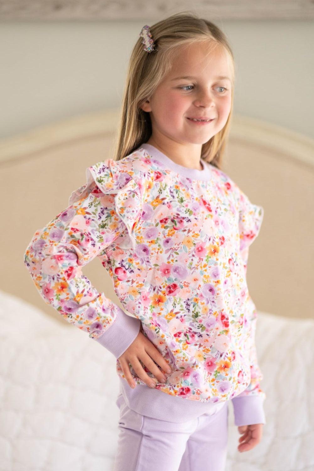 Girl wearing flower garden ruffle shoulder sweatshirt and lavender joggers, front-facing floral outfit for kids.