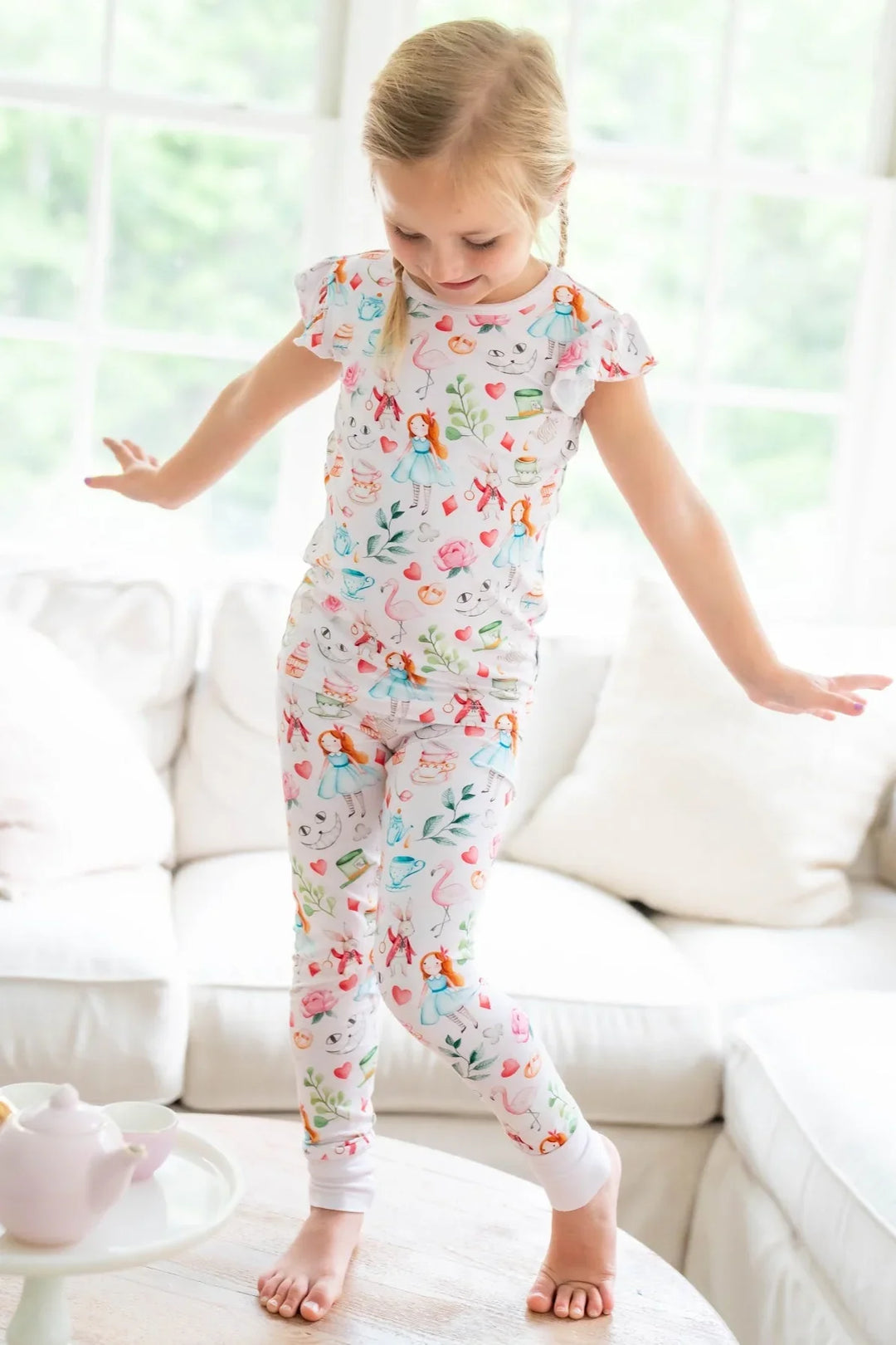 Little girl standing in Adventures with Alice bamboo pajama set with short sleeves and long pants, with tea cup design
