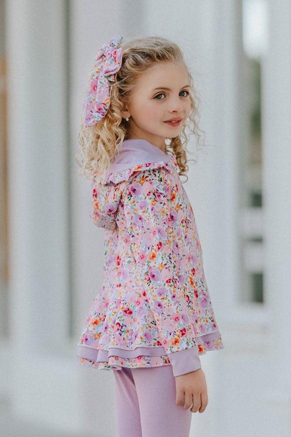Side view of girl wearing floral peplum jacket with layered ruffle hem and lavender cuffs, part of matching set.