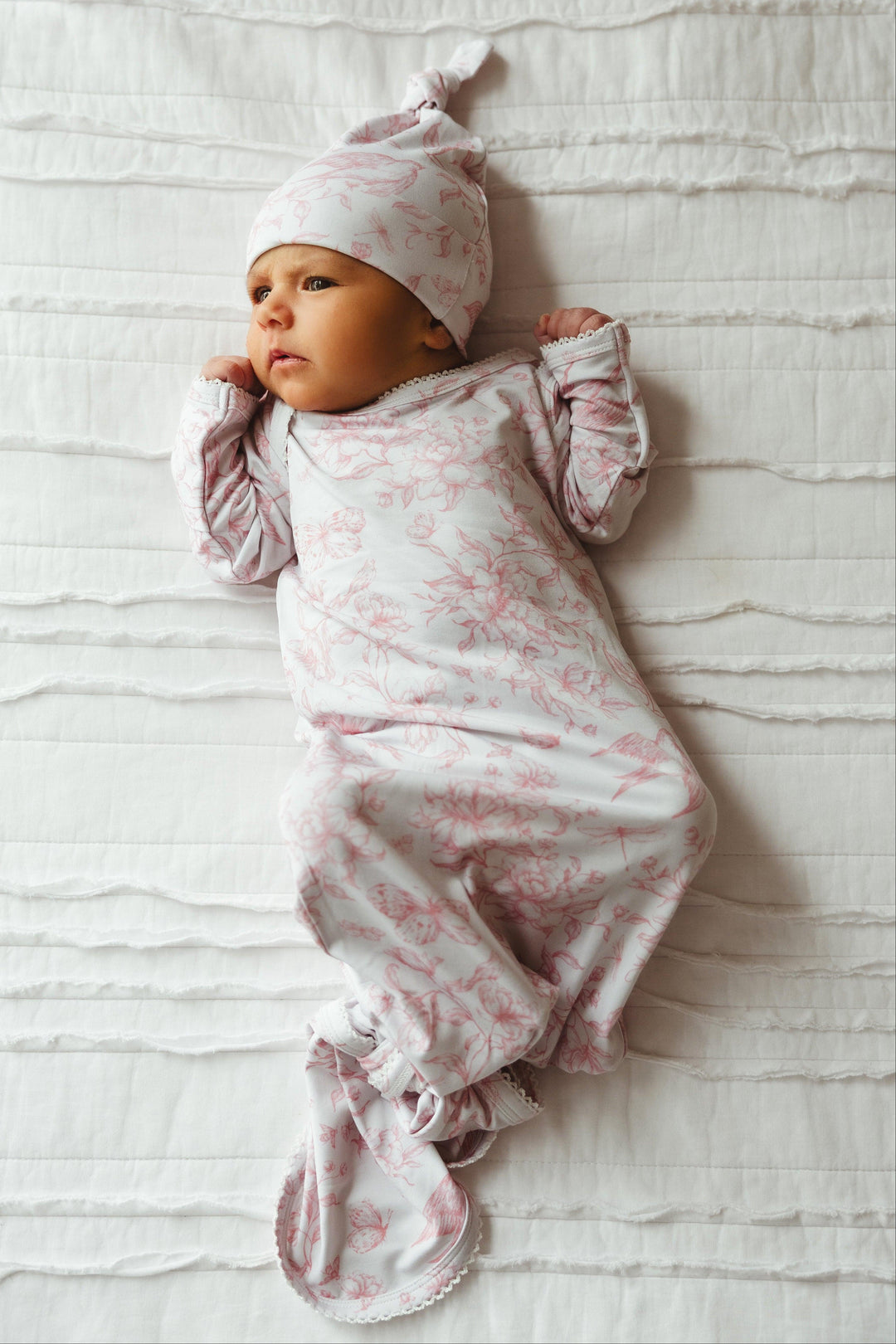 Newborn baby girl wearing Botanical Lullaby bamboo knotted gown, lying peacefully in nature-inspired rose and ivory print — soft, breathable, and perfect for first photos or gifting.