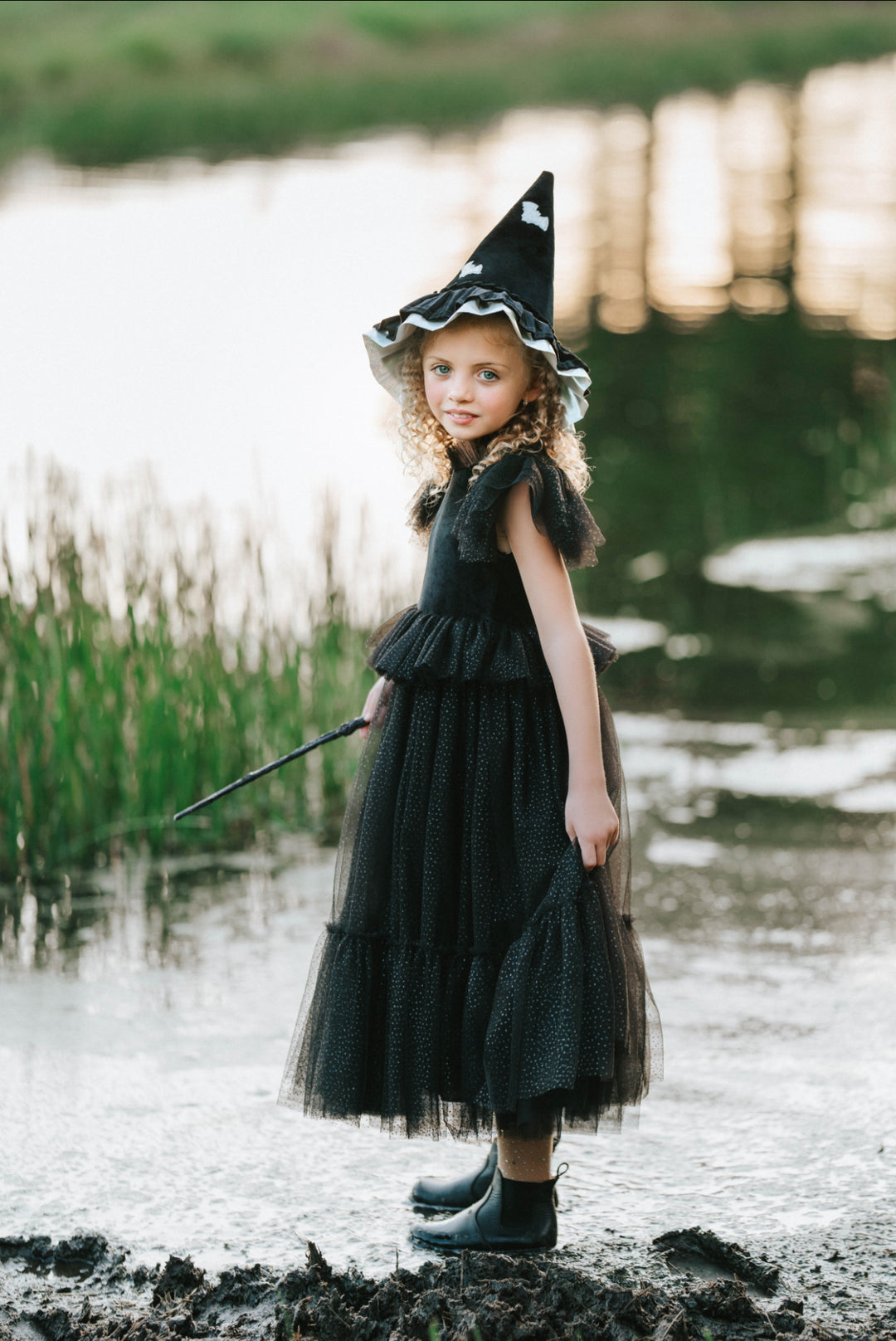 Child in black velvet witch dress holding wand and hat separately