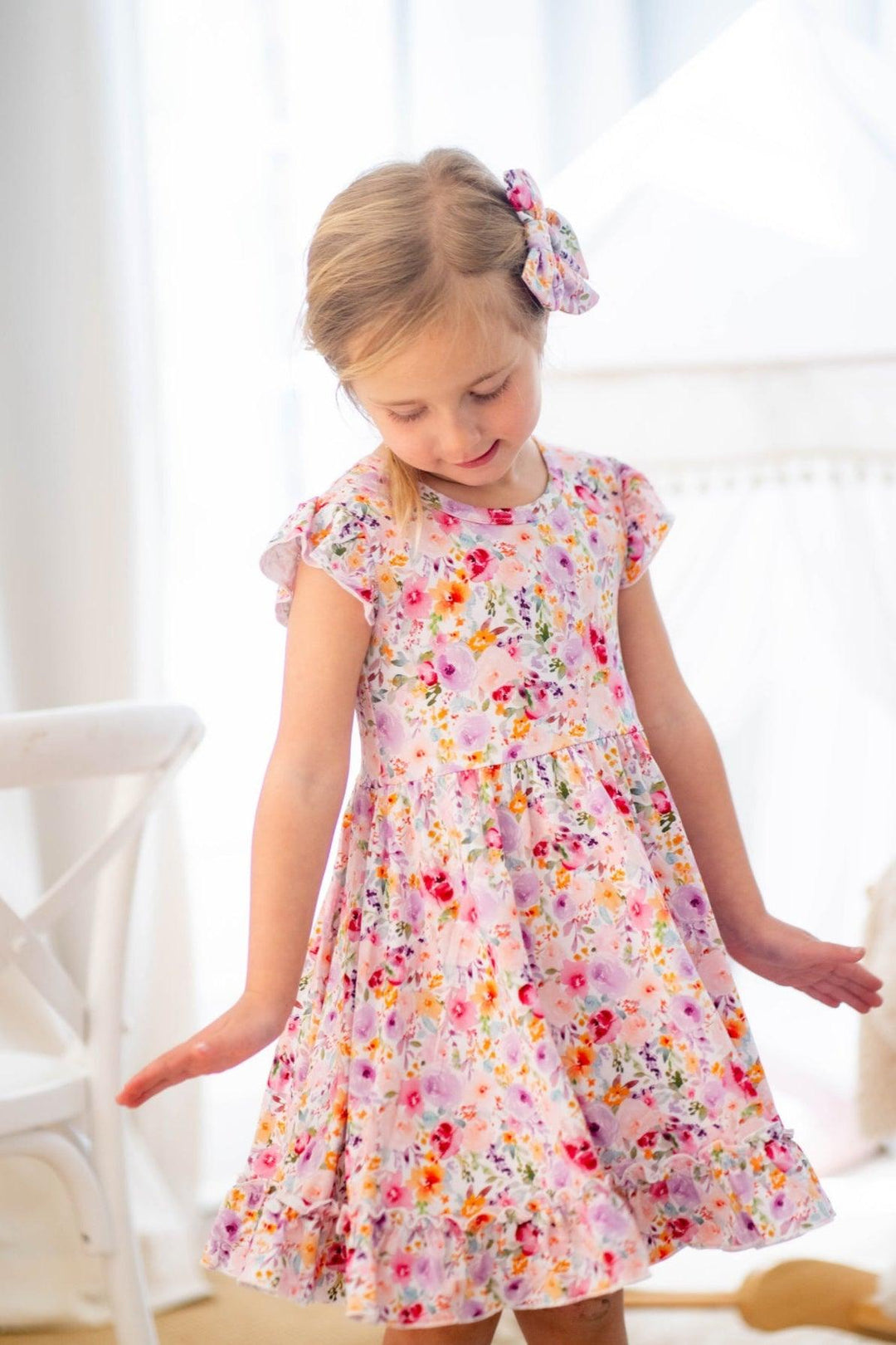 Girl modeling flower garden bamboo twirl dress with short ruffle sleeves and floral print, front-facing pose.