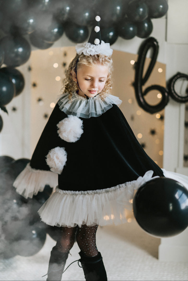 Child in vintage-inspired clown costume with lace-up boots and black balloons
