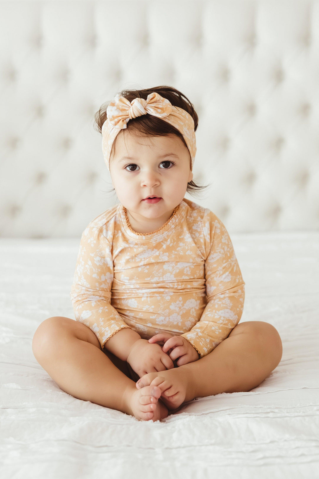 Baby girl sitting in Golden Afternoon floral bamboo bodysuit with long sleeves and scalloped edging — soft, breathable, and ideal for everyday wear or special photo moments.