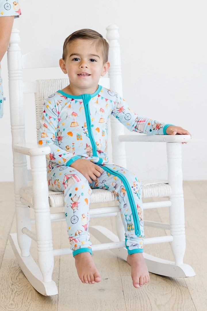 Toddler boy on rocking chair wearing circus print bamboo footed romper with convertible feet and dual zipper, ideal for cozy sleepwear