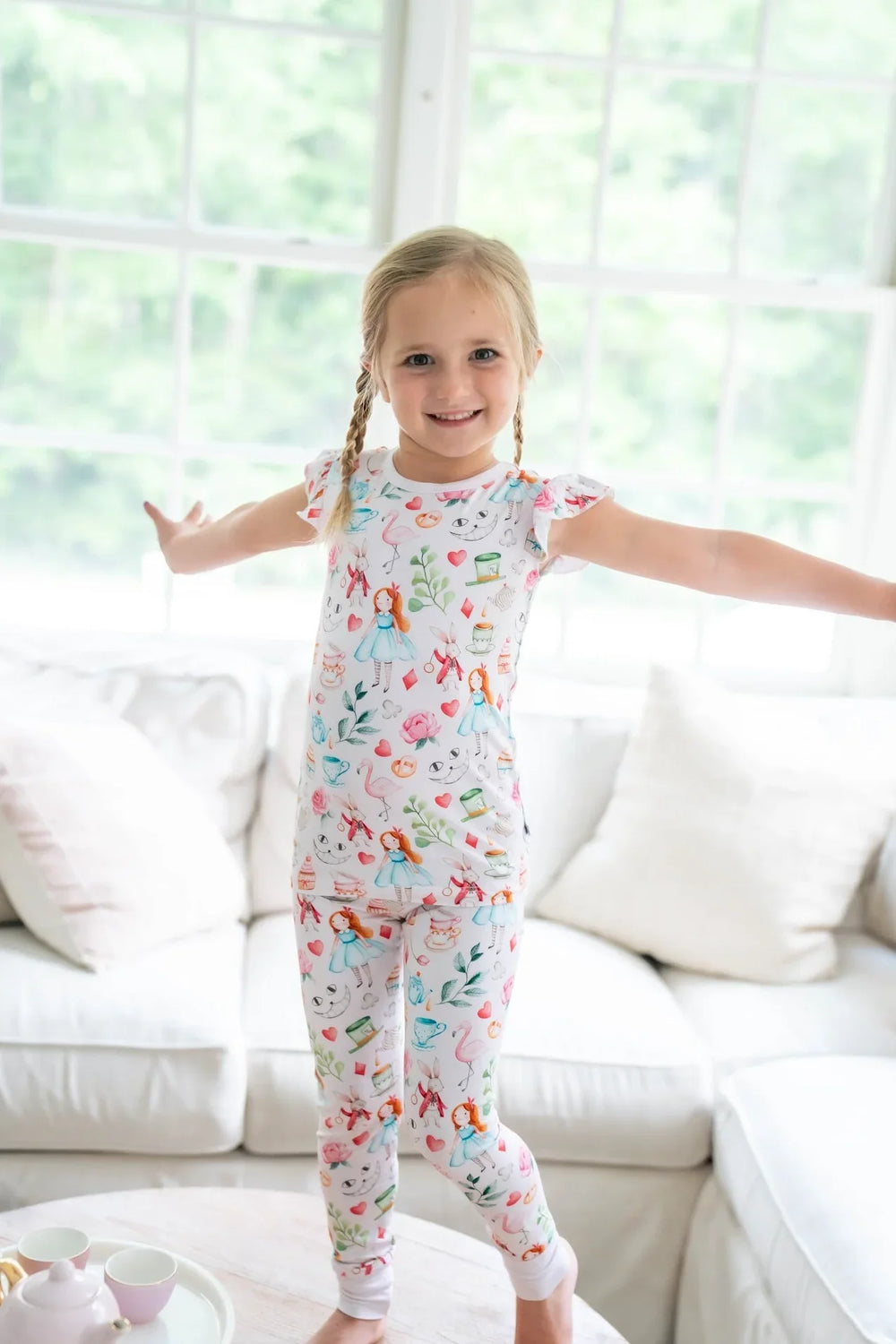 Adventures with Alice 2-piece bamboo sleepwear set. Girl modeling Alice in Wonderland print bamboo pajamas, shown in soft pink two-piece set.