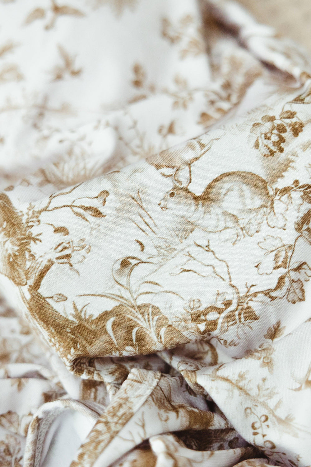 Close-up of Woodland Toile print on bamboo newborn gown, showing detailed forest animals including bears and foliage in soft brown tones on ivory fabric.
