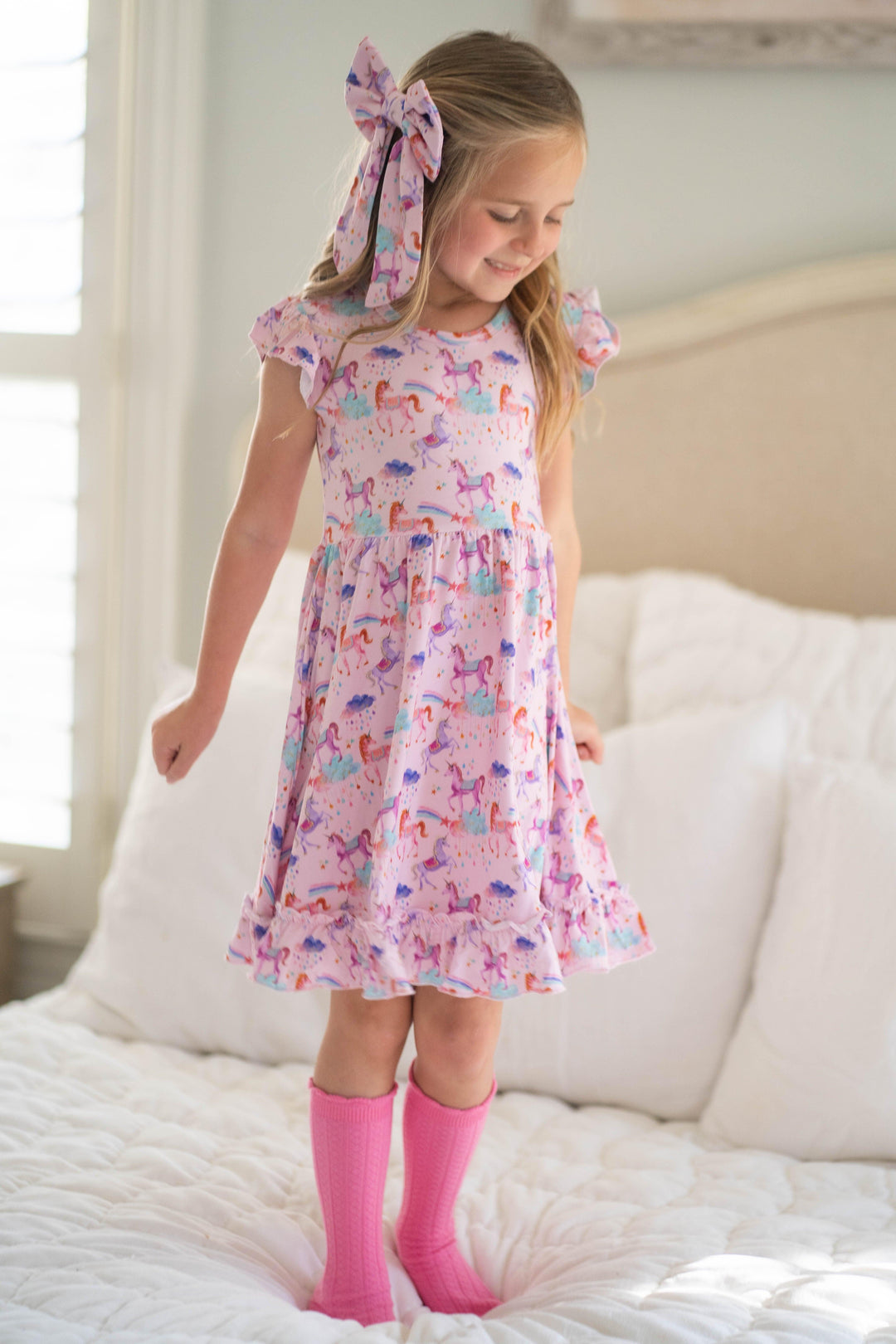 Little girl standing in Magical Unicorns twirl dress with short ruffle sleeves, styled with a matching bow — perfect for spring outfits or unicorn-themed events.