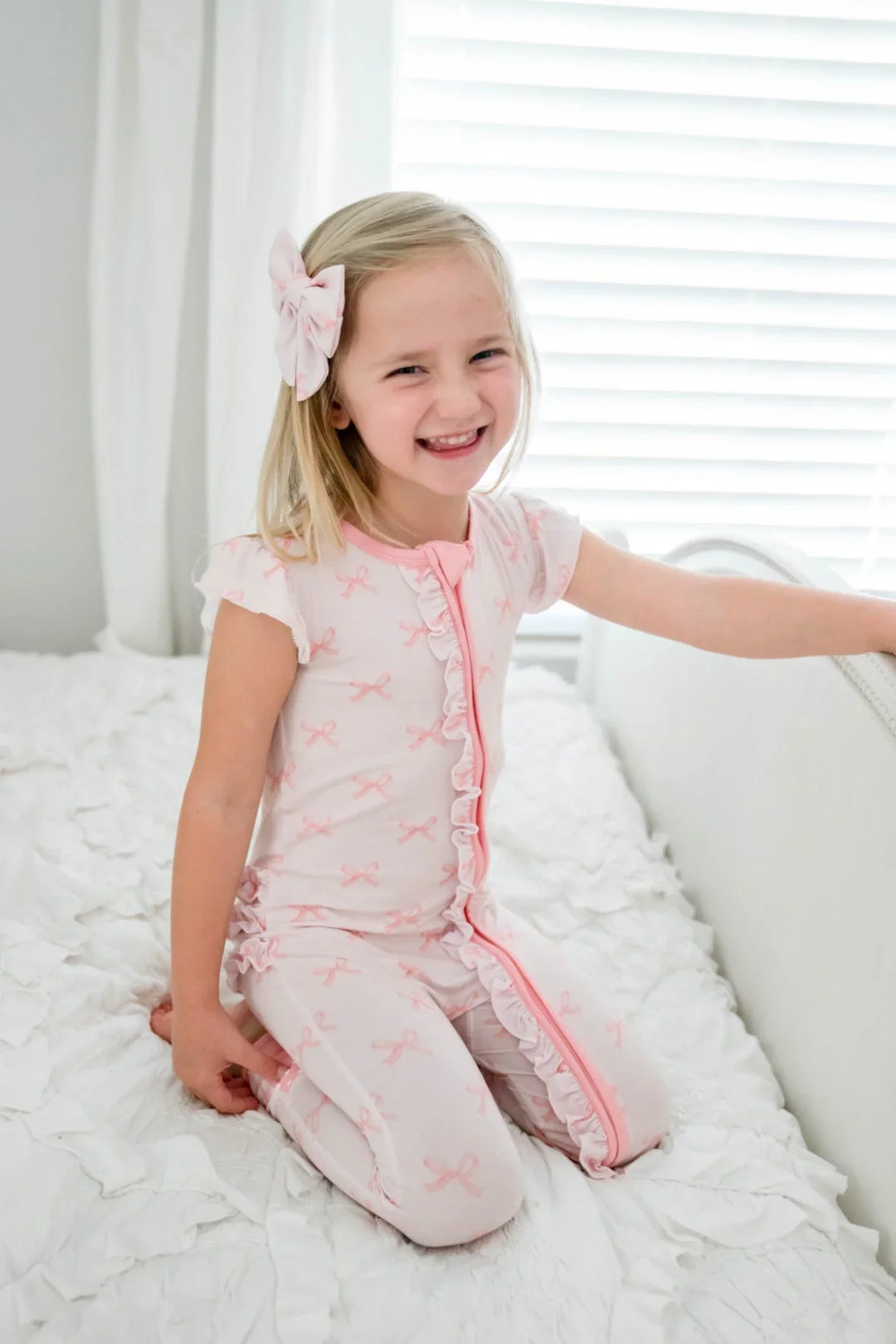 Little girl kneeling in pink bows bamboo zipper romper with short ruffle sleeves and convertible fold-over feet.