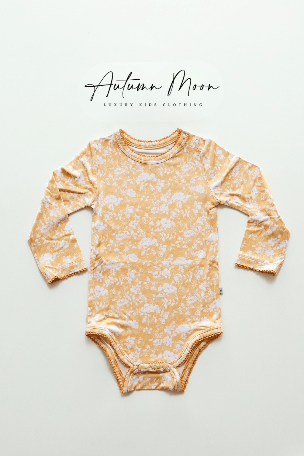 Flat lay of Golden Afternoon bamboo long sleeve baby bodysuit with snap bottom, featuring a golden yellow background with delicate white floral print and scalloped trim — made from buttery soft bamboo viscose, perfect for baby girls and gift registries.