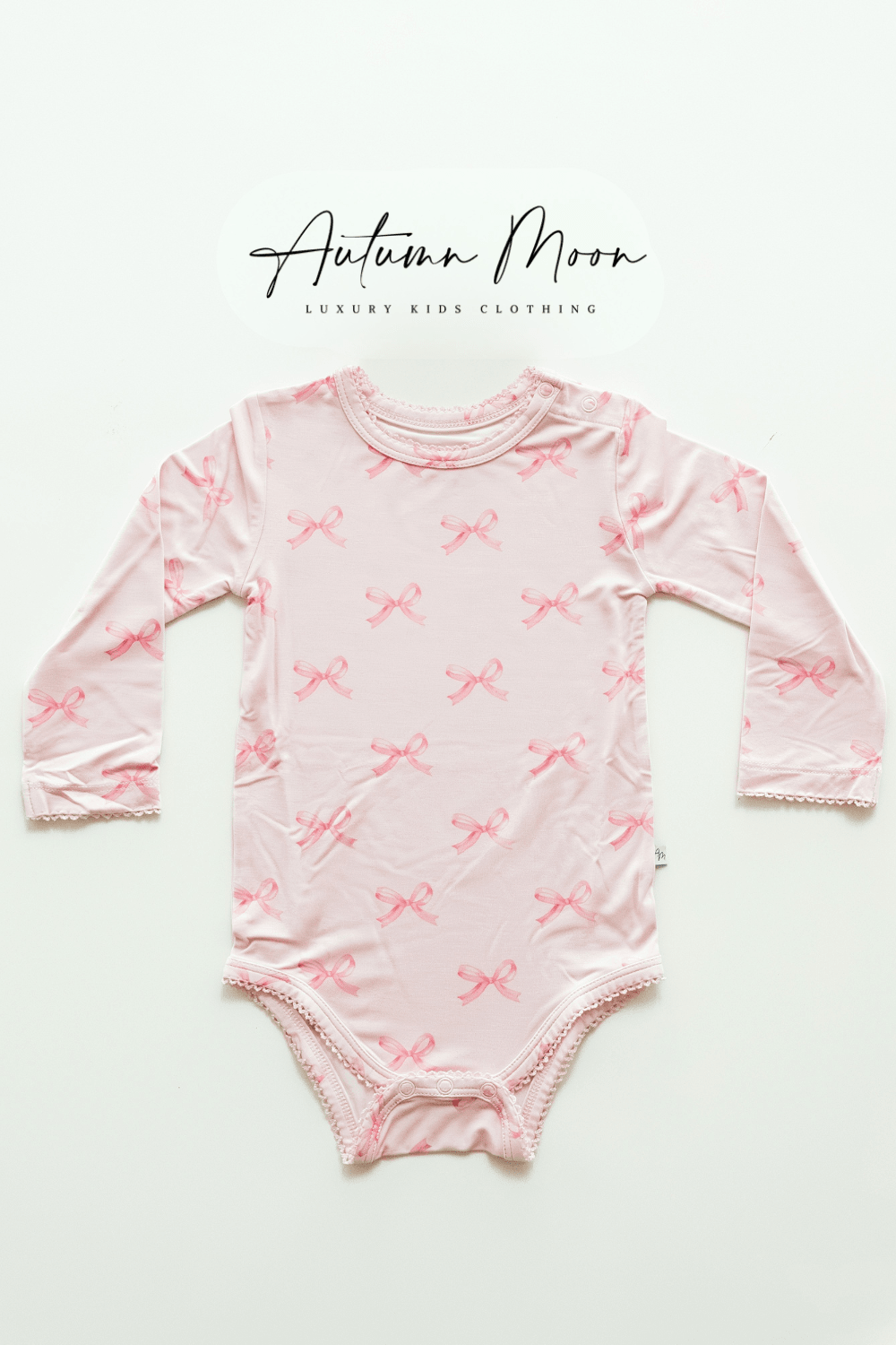 Flat lay of pink bows bamboo long sleeve baby bodysuit featuring a soft light pink background with darker pink bow print — made from buttery soft bamboo viscose, ideal for baby girls.