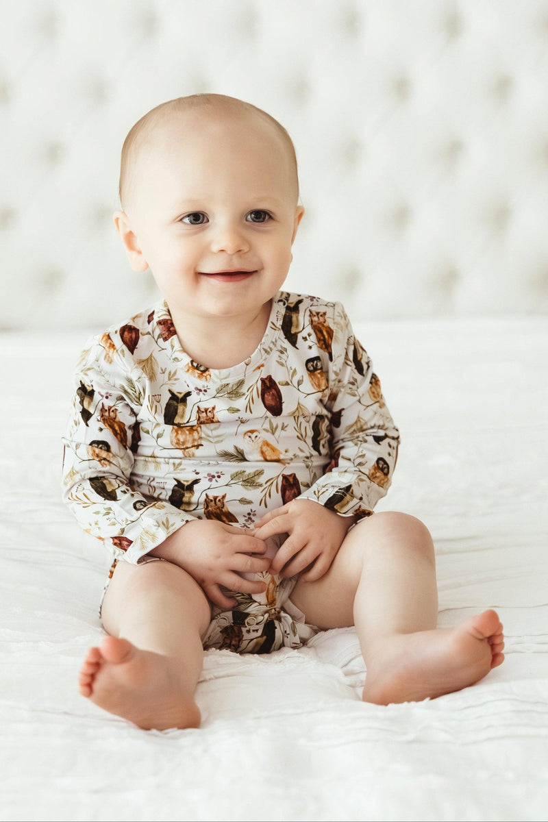 Front-facing baby sitting in Sleepy Hollow Owls bamboo bodysuit, smiling in cozy, unisex owl-themed outfit made for comfort and cuteness.
