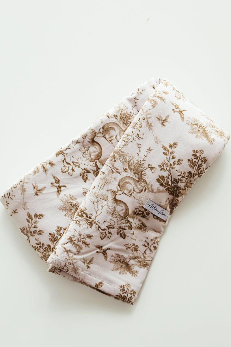 Flat lay of Woodland Toile bamboo newborn swaddle blanket, featuring a soft ivory background with detailed brown woodland animals like squirrels, birds, and deer — ultra-soft, breathable, and perfect for gender-neutral nurseries or baby shower gifts.