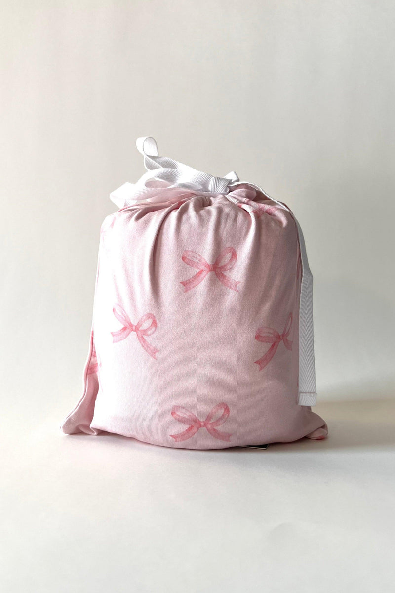 Pink Bows bamboo crib sheet neatly folded in matching drawstring pouch made from the same pink bow printed fabric — gift-ready and perfect for nursery organization or baby registries.