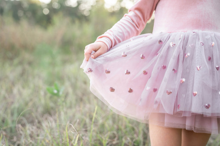 Girl standing indoors near window wearing rosewood velvet tutu dress, soft natural light.