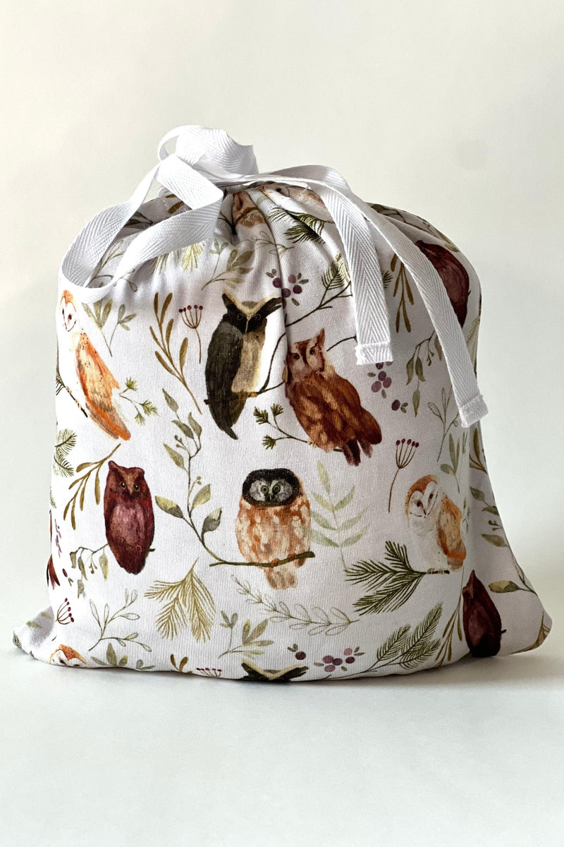 Sleepy Hollow Owls bamboo crib sheet folded inside coordinating fabric drawstring pouch, showcasing the adorable owl and greenery print — perfect for baby showers and nursery gift registries.