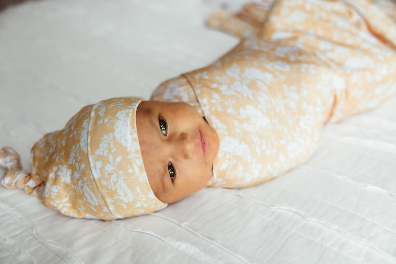 Newborn baby girl wrapped in Golden Afternoon floral bamboo swaddle blanket, peacefully resting in buttery soft fabric designed for soothing comfort — ideal for hospital photos, swaddling, and luxury nursery essentials.