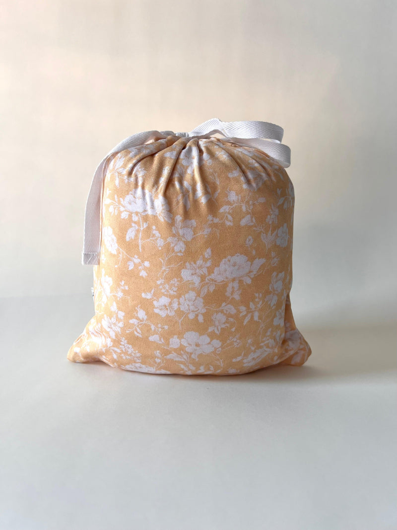 Golden Afternoon floral crib sheet neatly folded inside matching drawstring pouch, made from the same bamboo fabric — gift-ready and perfect for baby registries or new mom bundles.
