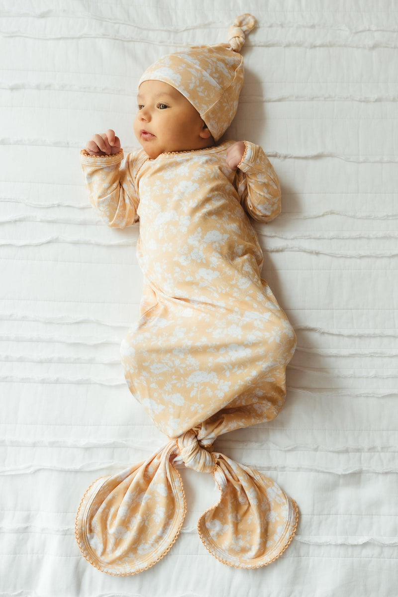 Newborn baby girl wearing Golden Afternoon bamboo knotted gown, featuring a golden yellow background with delicate white floral print and feminine scalloped edging — soft, breathable bamboo viscose ideal for newborn photos, baby showers, and hospital take-home outfits.
