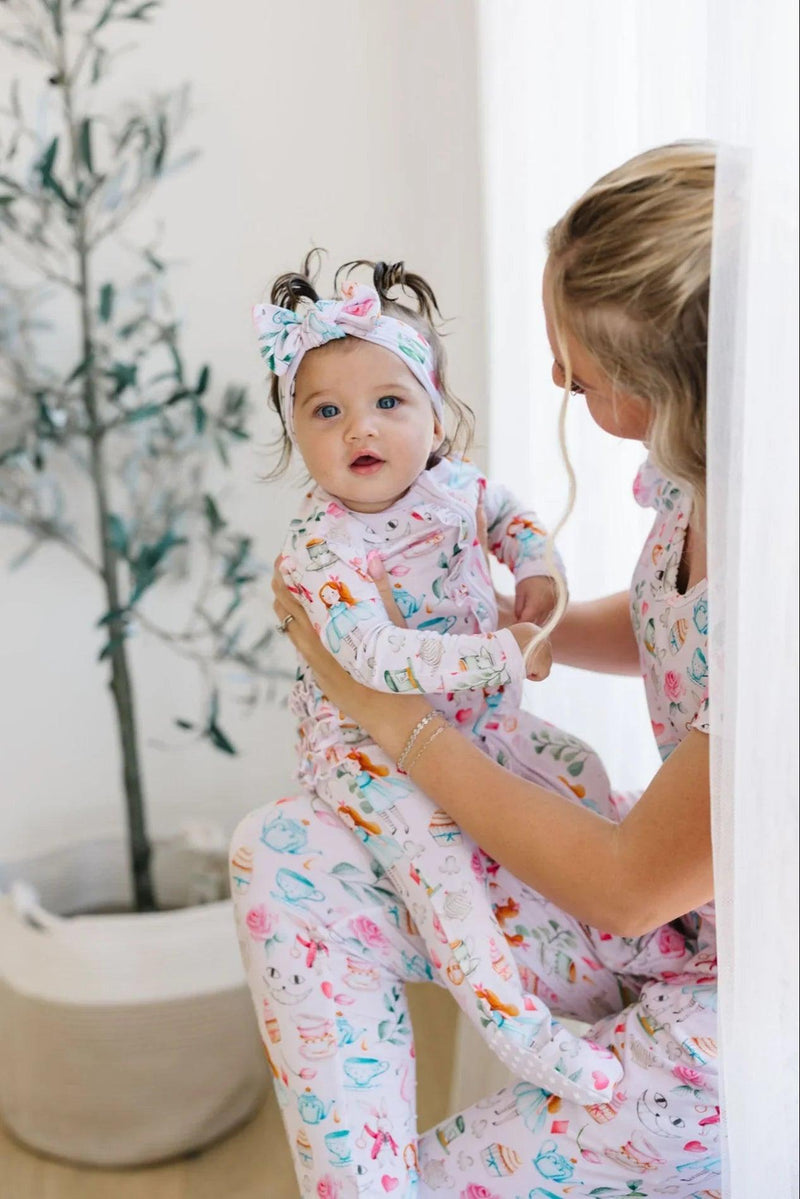 Mom and baby in matching Adventures with Alice bamboo pajamas, featuring pink print with teacups and Cheshire Cat.