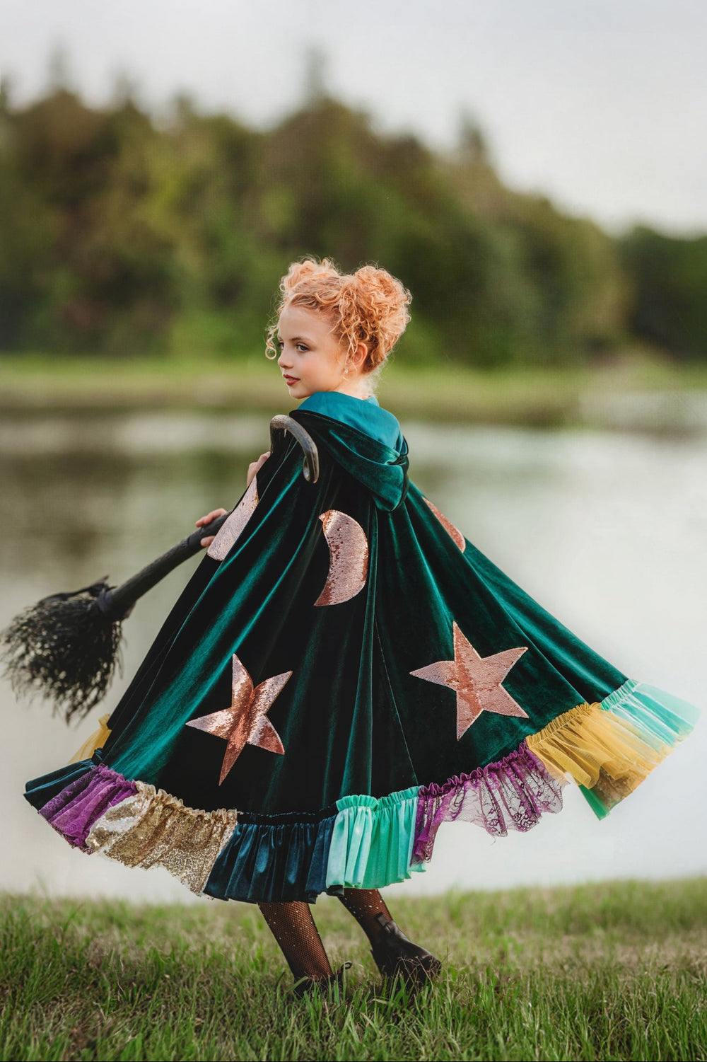 Girl twirling in green velvet witch cape with multicolor ruffle trim.