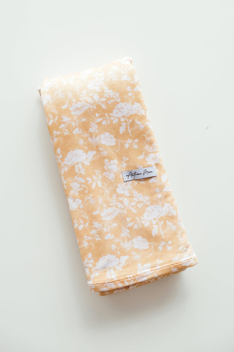 Flat lay of Golden Afternoon bamboo baby swaddle blanket featuring a rich golden yellow background with delicate white floral print — made from ultra-soft, breathable bamboo viscose, perfect for baby girls, newborn gifting, and registry must-haves.