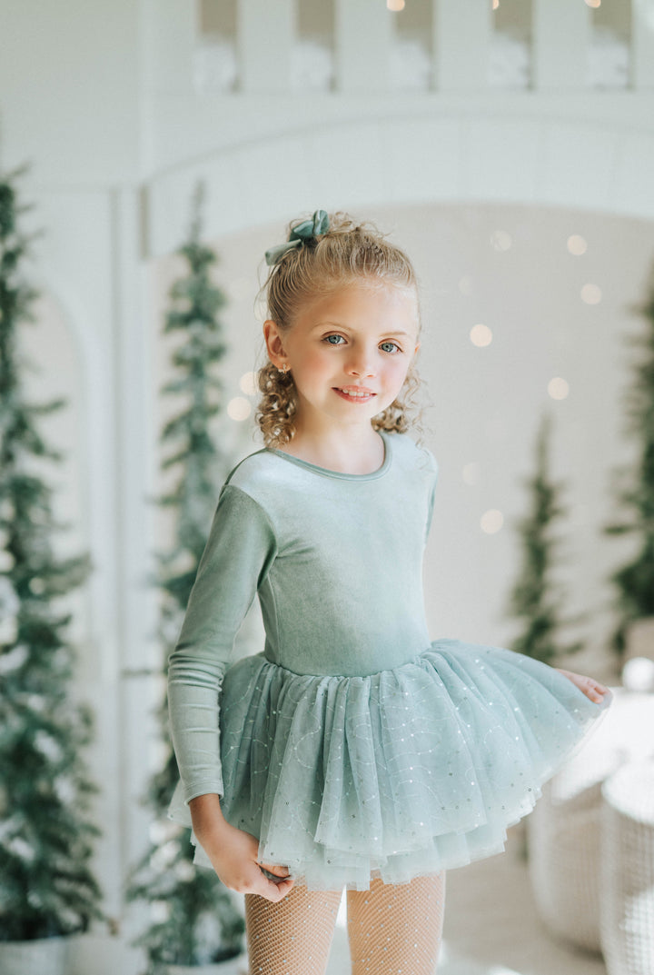 Young girl in a green ballet outfit standing in a decorated room with Christmas trees.