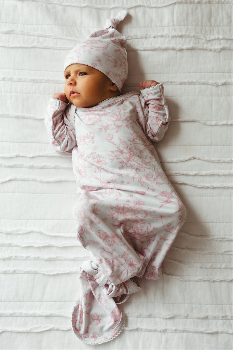 Newborn baby girl wearing Botanical Lullaby bamboo knotted gown, lying peacefully in nature-inspired rose and ivory print — soft, breathable, and perfect for first photos or gifting.

