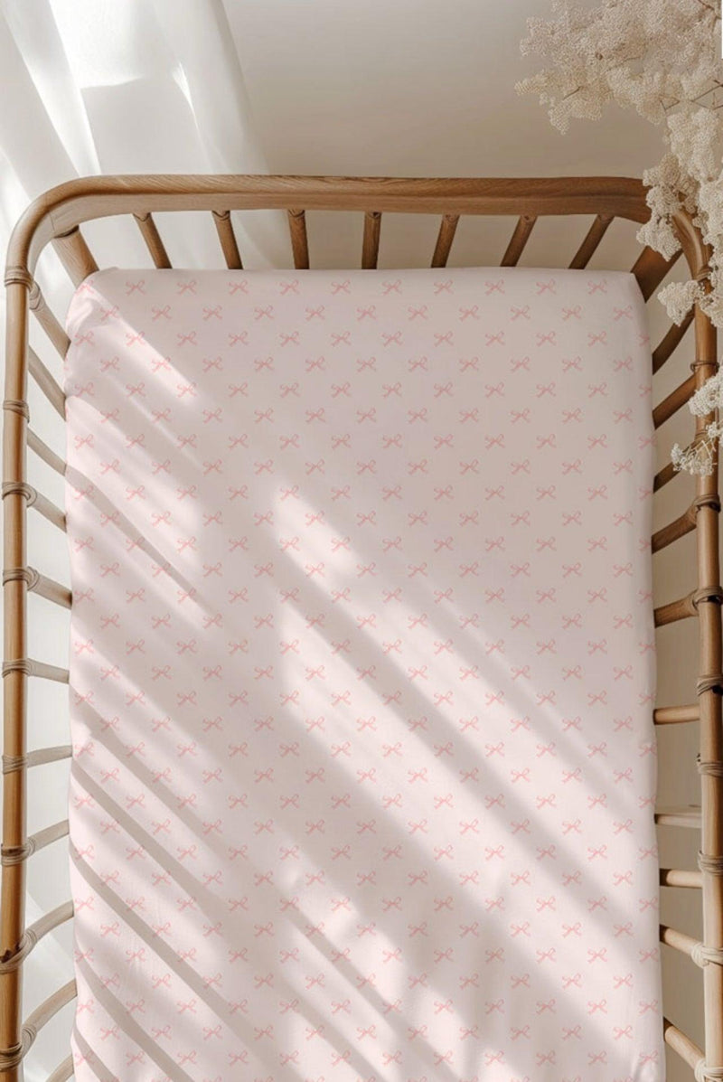 Pink Bows bamboo crib sheet on a standard crib mattress, featuring a soft light pink background with darker pink bow print — breathable, hypoallergenic, and perfect for baby girl nurseries.