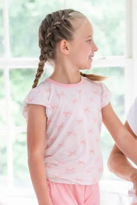 Little girl styling pink bows bamboo graphic T-shirt and ruffle shorts, shown with coordinating accessory.
