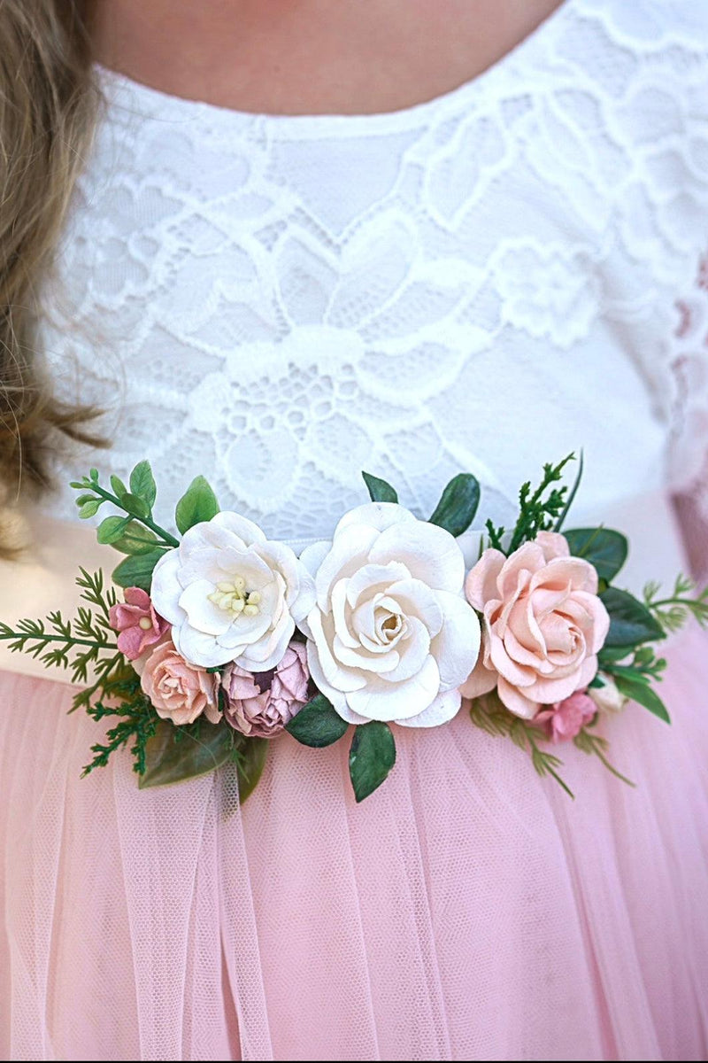 Floral sash with white and pink flowers on a person wearing a white lace top and pink tulle skirt.