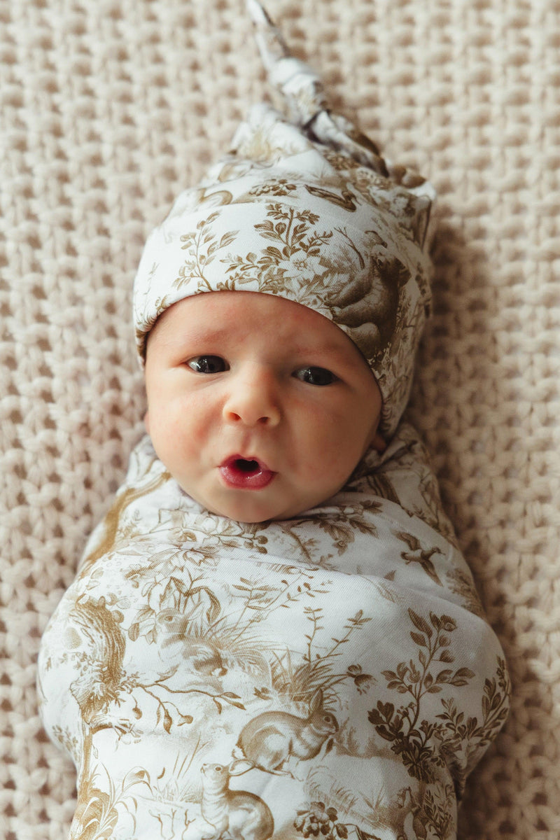 Newborn baby wrapped snugly in Woodland Toile bamboo swaddle blanket, showing cozy fit and neutral brown forest animal print — ideal for swaddling and newborn photography.