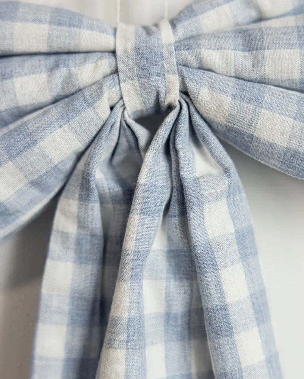 Close-up of handcrafted baby blue gingham fabric bow with classic cotton detailing.