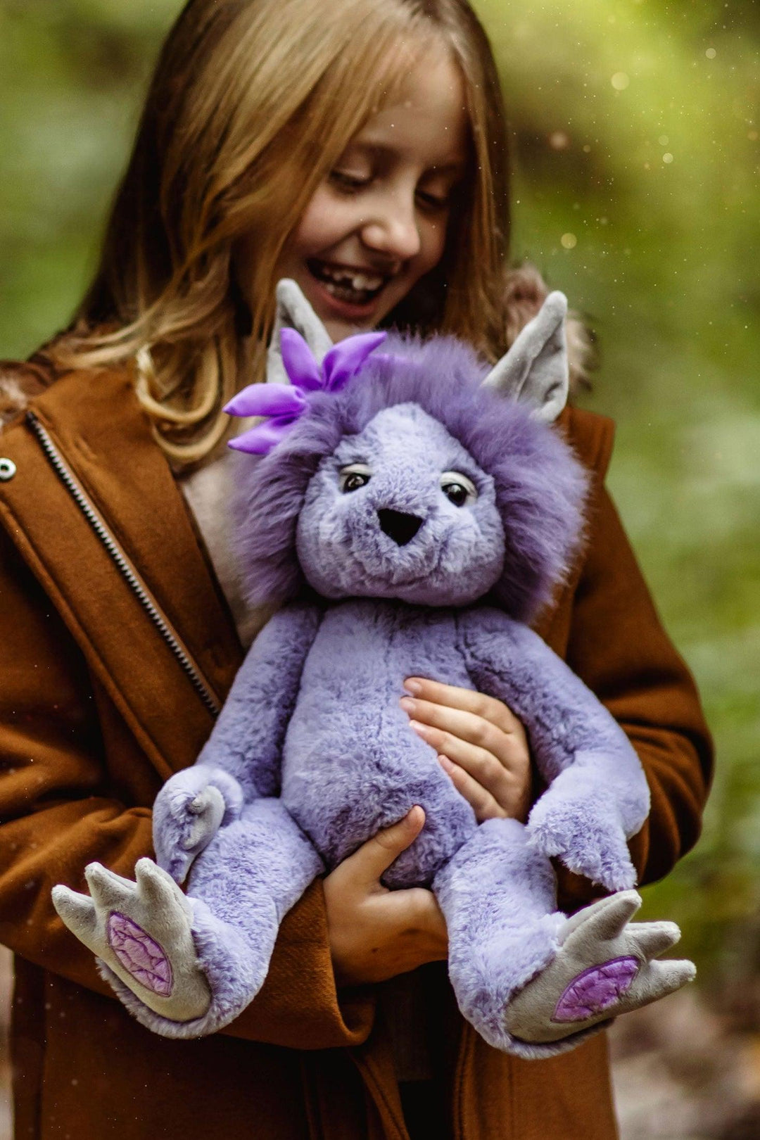 Amethyst Boo Crystal Troll by Charlie Bears held by a child in a woodland setting with lavender plush and purple flower detail