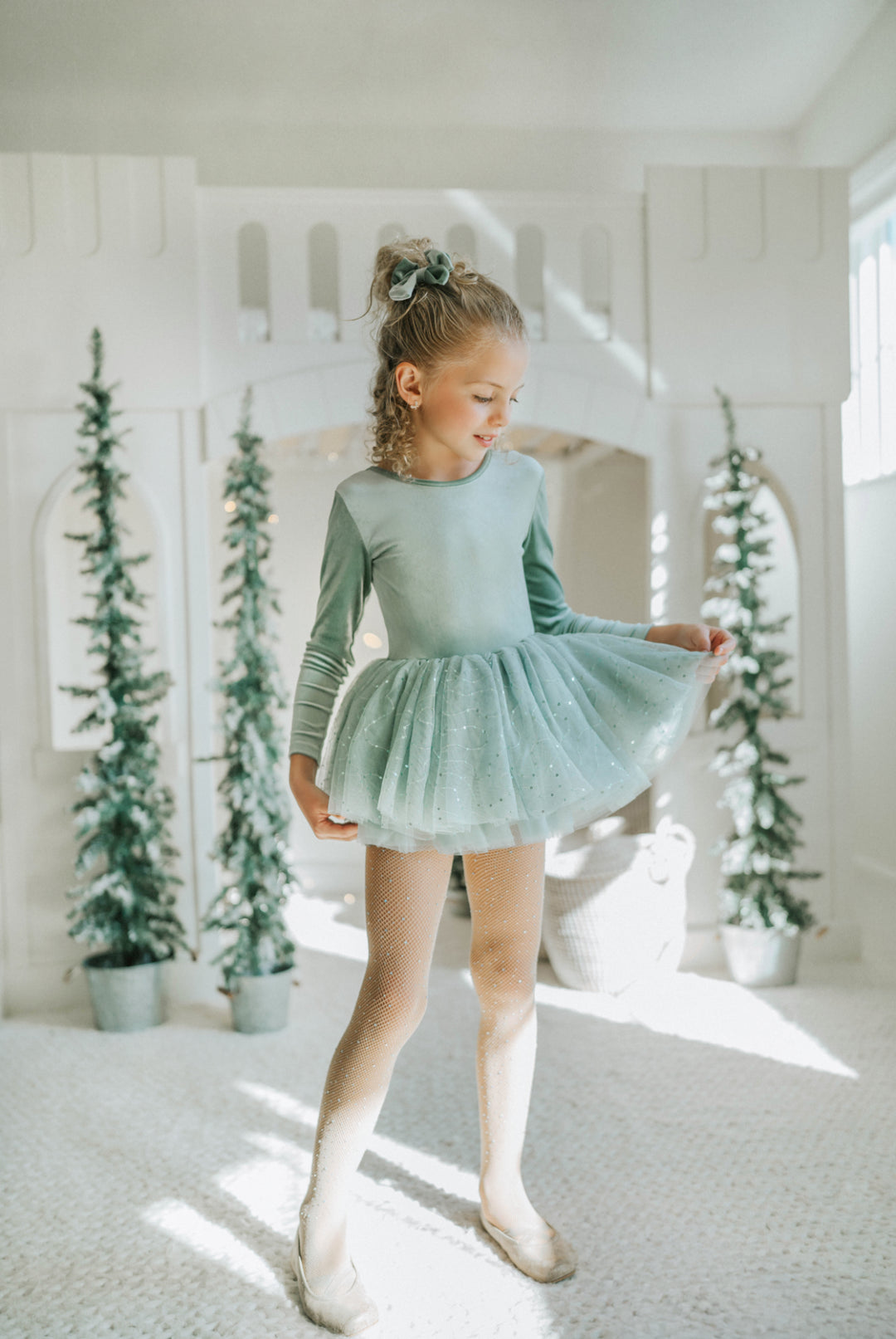 Young girl in a sage green tutu dress standing in a room with decorative plants.
