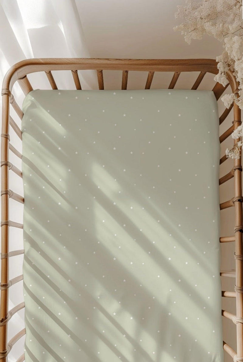 Sage green bamboo crib sheet with off-white scattered stars, fitted on a standard crib mattress — soft, breathable, and perfect for gender-neutral nurseries.
