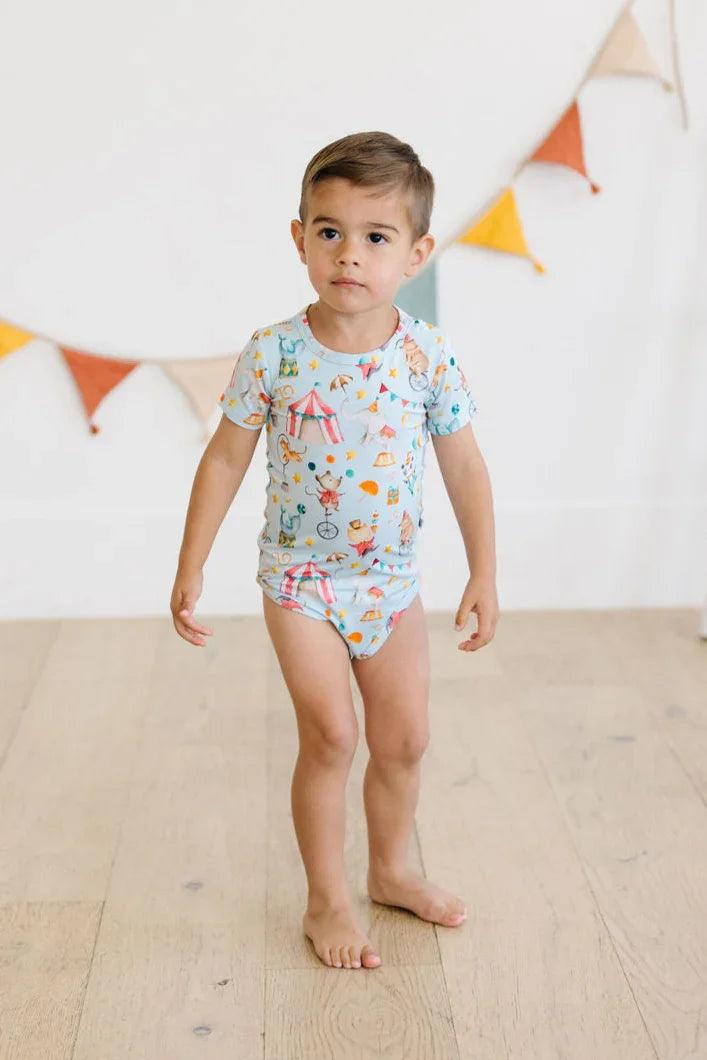 Toddler boy standing in Take Me to the Circus short sleeve bamboo bodysuit, snap bottom style for easy changes.