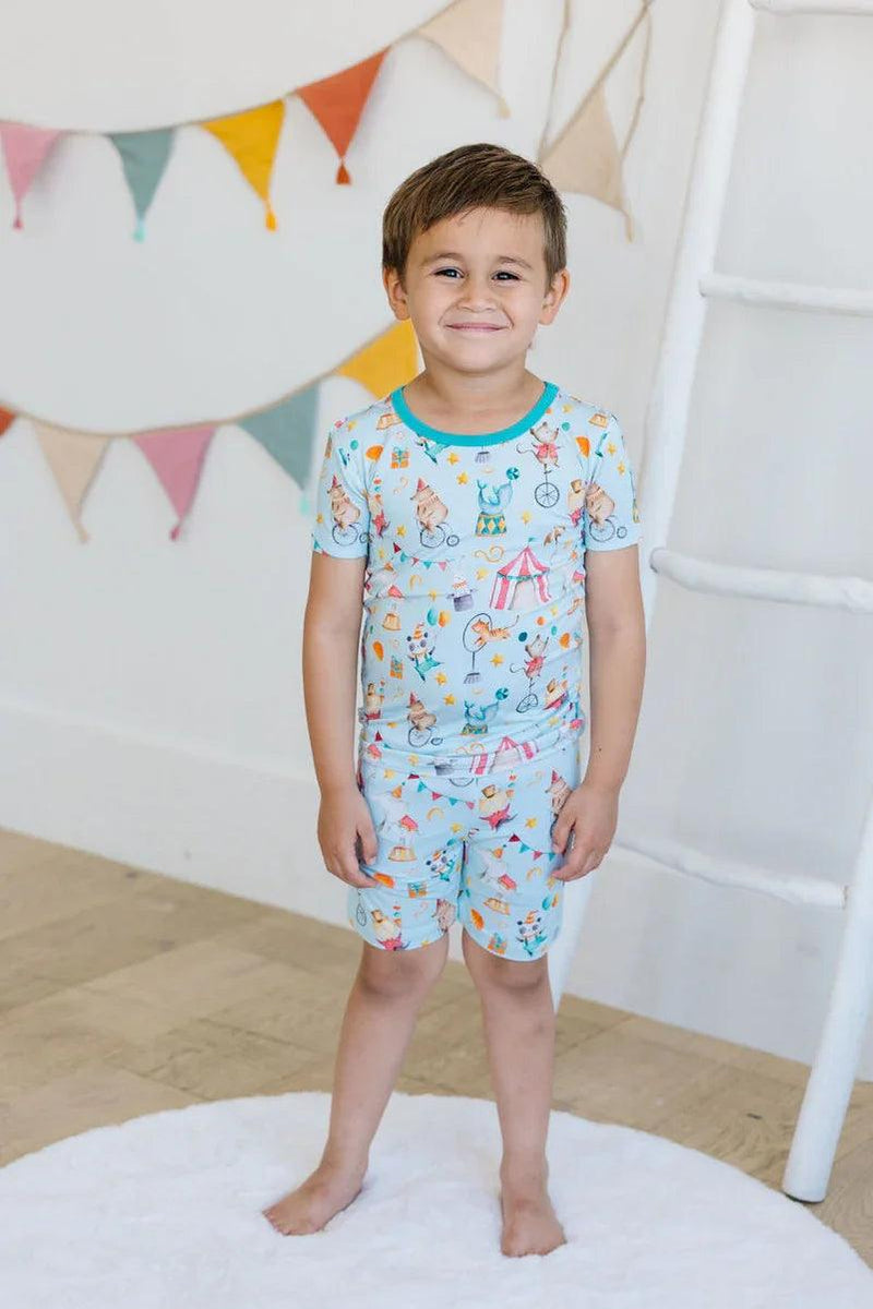 Little boy standing in circus print bamboo two-piece pajamas, short sleeve top and shorts shown front-facing.