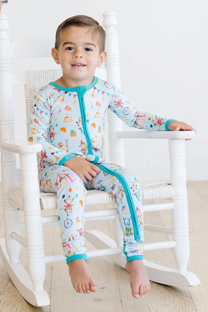 Toddler boy on rocking chair wearing circus print bamboo footed romper with convertible feet and dual zipper, ideal for cozy sleepwear
