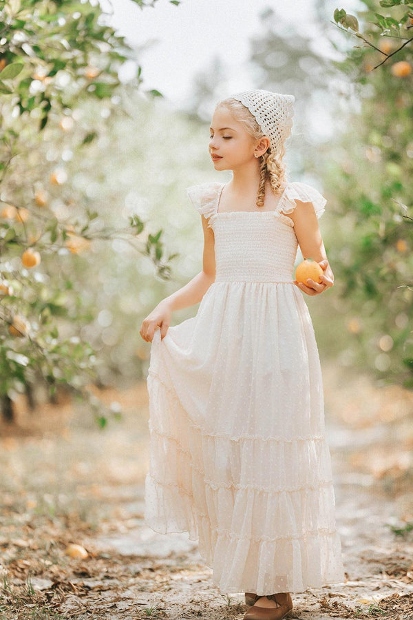 Girl wearing the Citrus Cream Orchard Dress walking through a sunlit orchard holding fresh fruit in a flowing heirloom-inspired dress