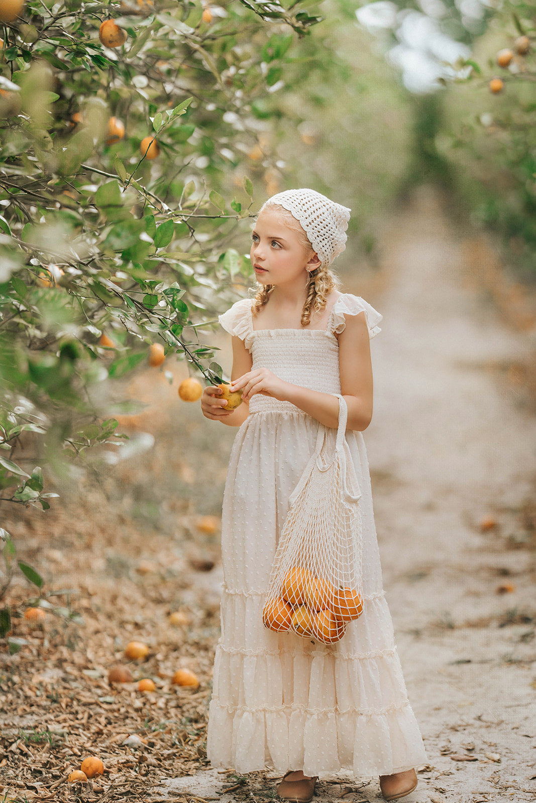 Child wearing the Citrus Cream Orchard Dress standing in an orchard with a basket of fruit and soft flutter sleeves