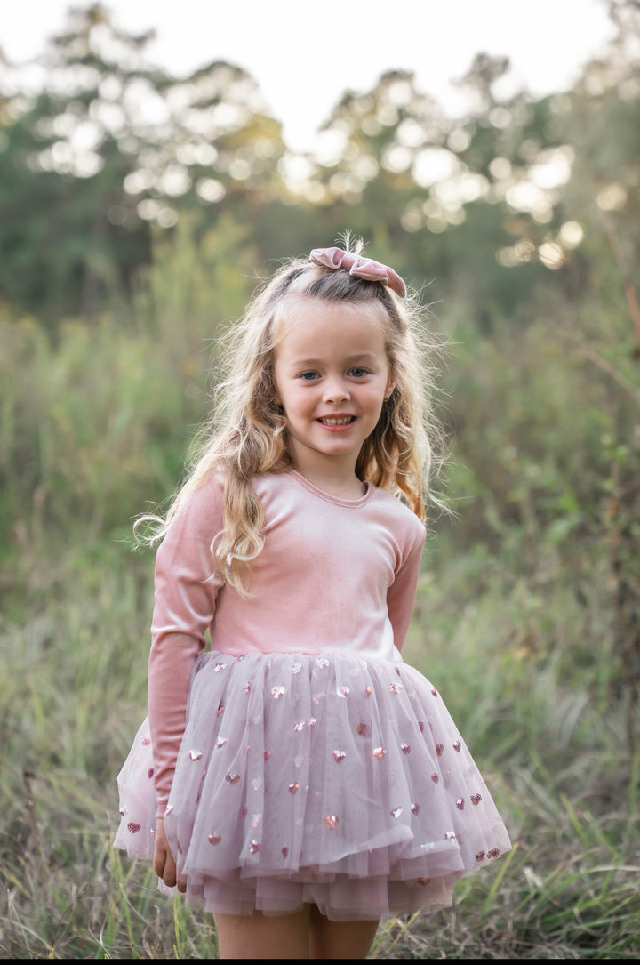 Girl smiling outdoors in rosewood velvet tutu dress, standing in grassy field.